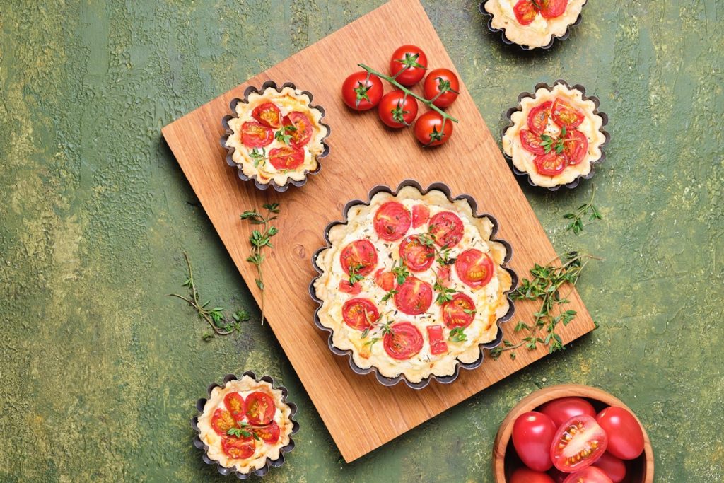 Cinci mini tarte cu roșii și brânză decorate cu cimbru, alături de roșii proaspete și crenguțe de cimbru