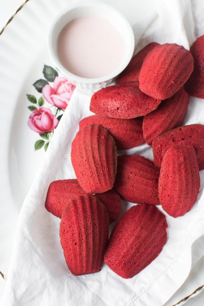 Madeleine Red Velvet pe un platou alb, alături de o ceașcă cu lapte