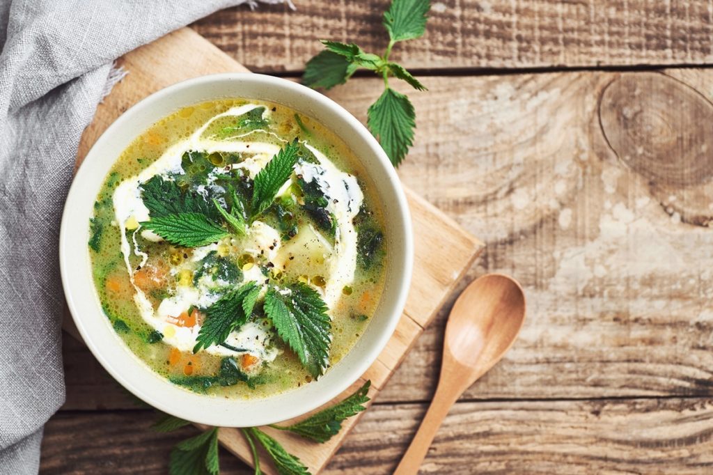 Ciorbă de urzici cu legume și smântână în bol, alături de lingură de lemn