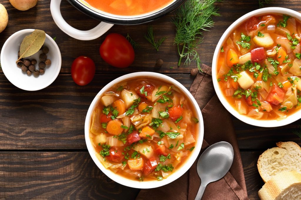 Două porții de ciorbă de varză albă cu cartofi, morcovi și roșii