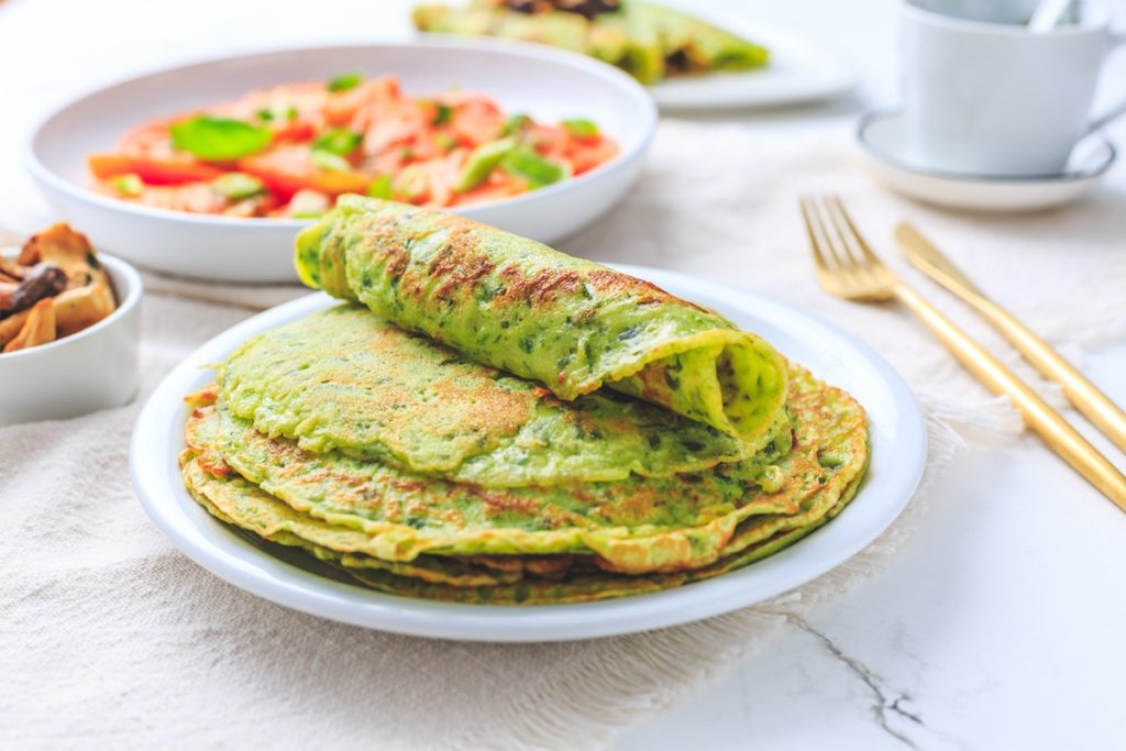 Clătite de post din cartofi, cu usturoi verde și ceapă verde pe o farfurie cu furculiță, alături de un bol cu salată de legume