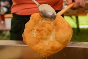 Gogoașă scoasă din ulei cu o lingură și o spatulă de lemn