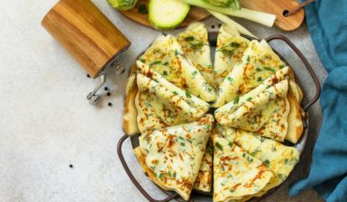 Clătite subțiri din dovlecei cu verdețuri de primăvară pe un platou, alături de o râșniță, dovlecei și ceapă verde