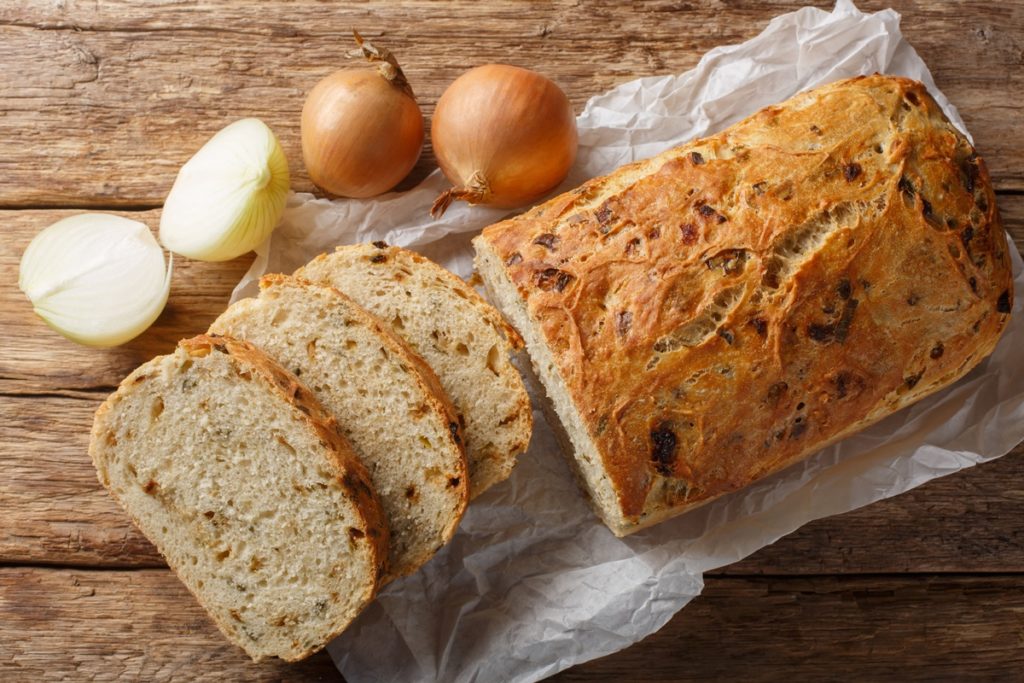 Pâine umplută cu ceapă caramelizată porționată pe o hârtie de copt, alături de ceapă