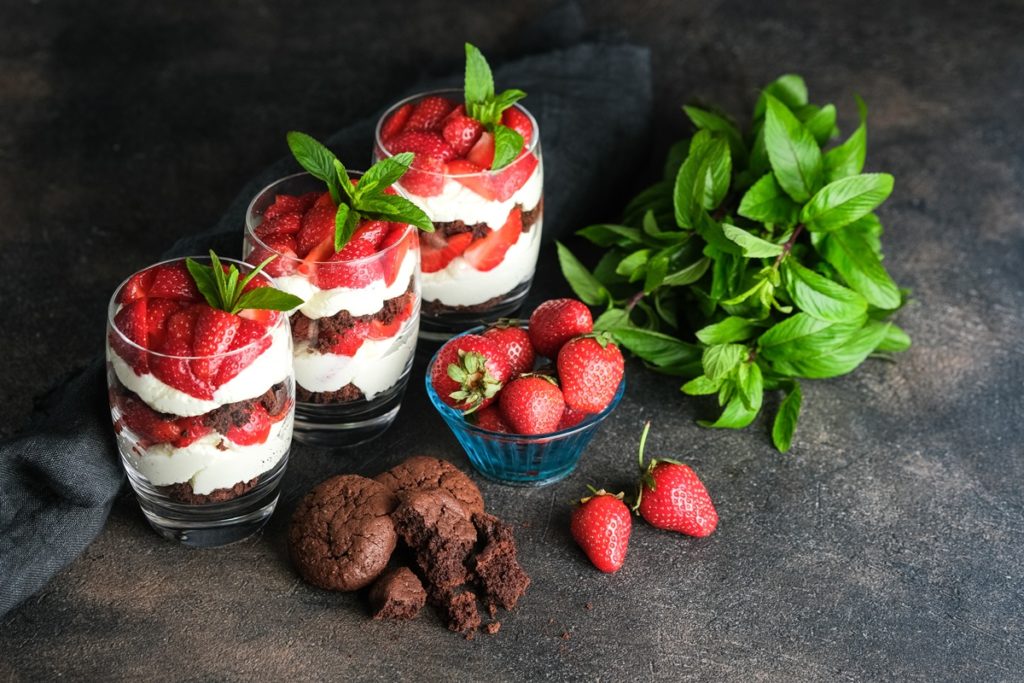 Trei pahare cu Trifles cu căpșuni și biscuiți cu ciocolată, alături de frunze de mentă, biscuiți și căpșuni