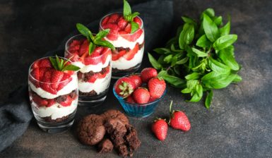 Trei pahare cu Trifles cu căpșuni și biscuiți cu ciocolată, alături de frunze de mentă, biscuiți și căpșuni