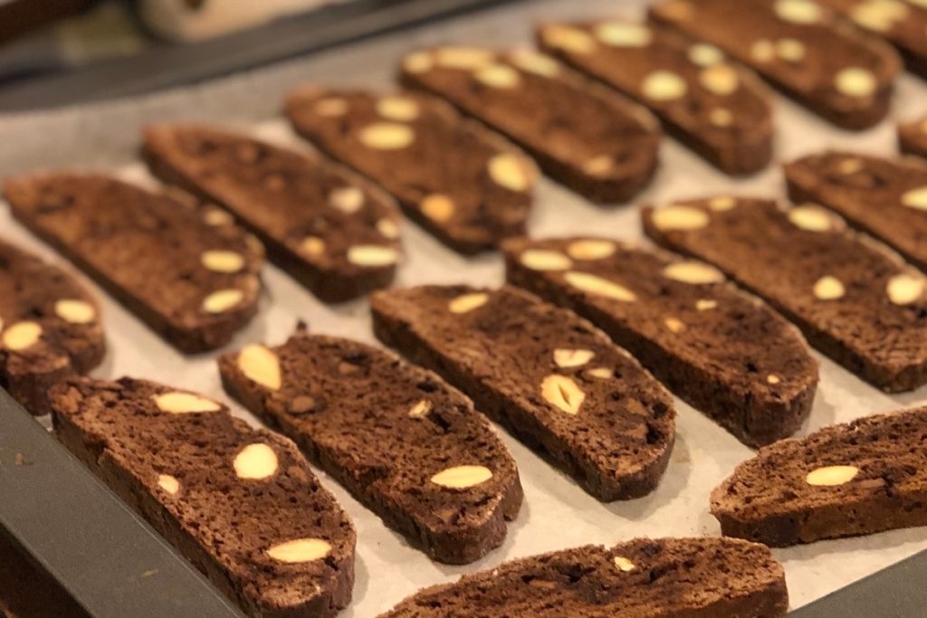 Biscotti cu alune și ciocolată în aluat așezați în tavă pentru a doua coacere