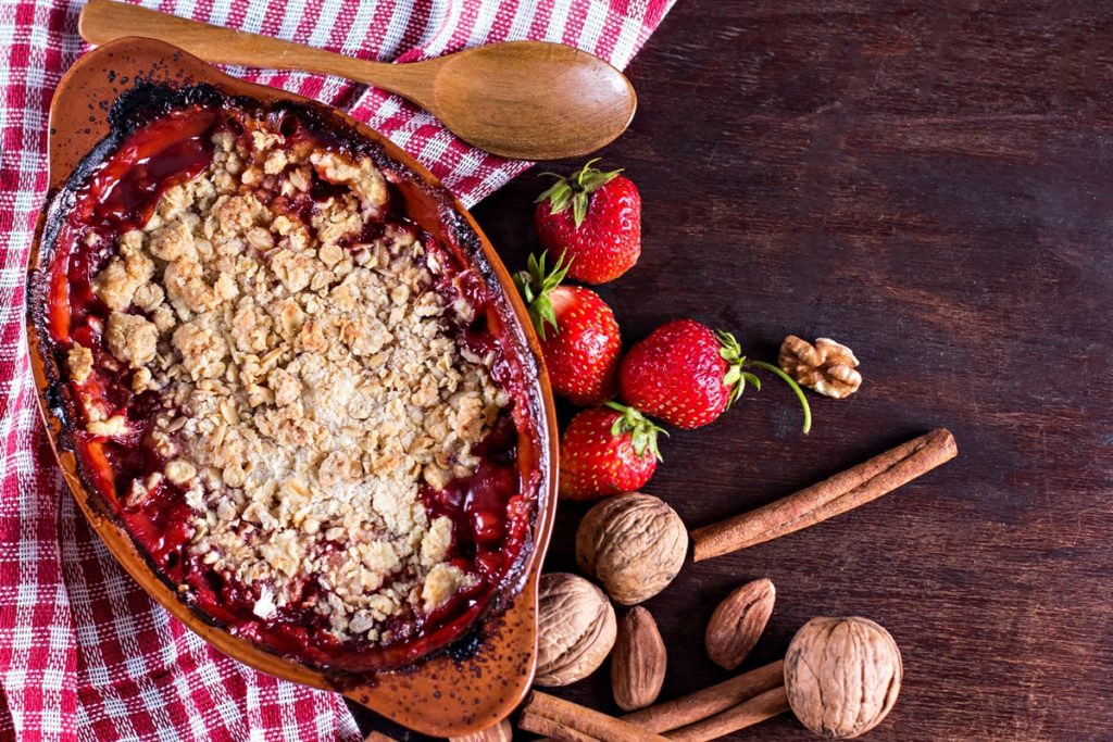 Cobbler cu rubarbă, căpșuni și migdale în vas de lut, alături de căpșuni, migdale și batoane de scorțișoară