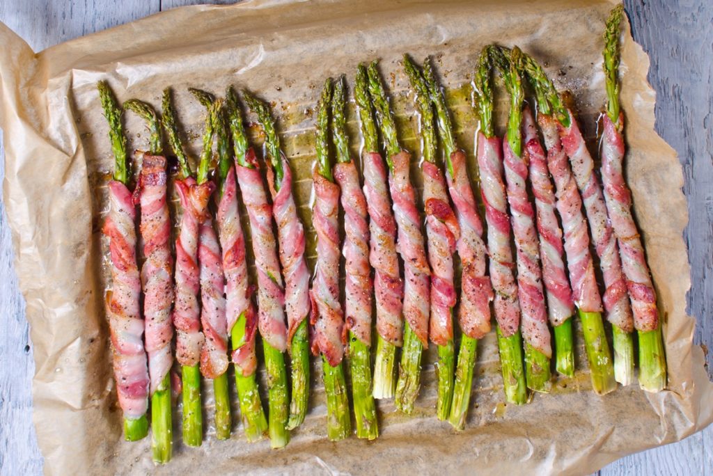 Sparanghel înfășurat în bacon într-o tavă, pe hârtie de copt