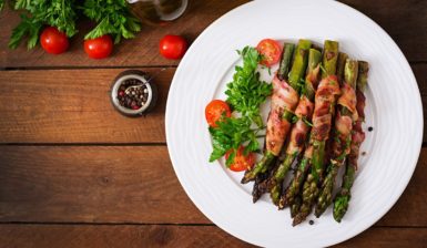 Sparanghel înfășurat în bacon pe o farfurie cu roșii cherry și verdeață