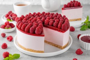 Cheesecake cu jeleu de zmeură secționat pe platou și o porție pe farfurie