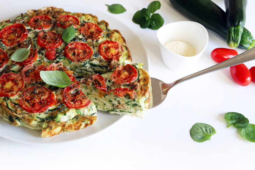 Frittata cu dovlecei și roșii, aromată cu busuioc, porționată pe o spatulă