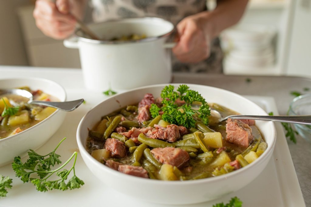 Mâncare de fasole verde cu carne și cartofi în două boluri și în oală