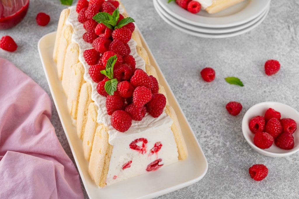 Prăjitură cu iaurt și zmeură decorată cu zmeură și frunze de mentă