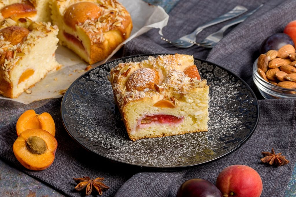 Porție de prăjitură umedă cu caise și nectarine, decorată cu migdale