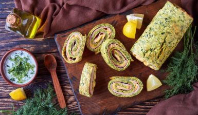 Ruladă din omletă cu dovlecei, umplută cu șuncă și cașcaval, porționată pe un tocător de lemn