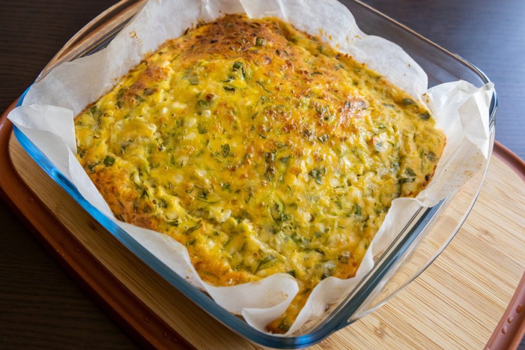 Budincă de dovlecei cu multe verdețuri într-un vas de yena cu hârtie de copt