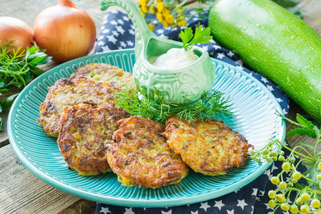 Chiftele de cartofi cu dovlecei și morcovi alături de un bol cu sos de iaurt