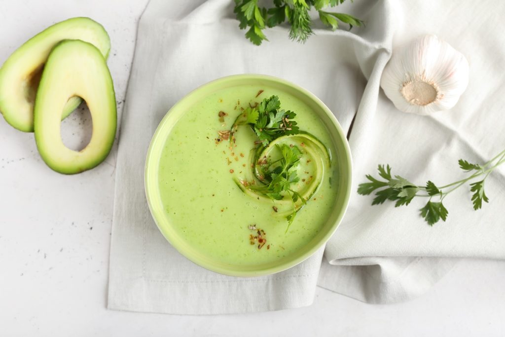 Gazpacho de avocado în bol, alături de felii de avocado și frunze de coriandru