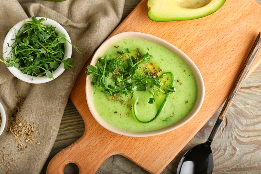 Gazpacho de avocado în bol, decorat cu ierburi, condimente și felii de avocado
