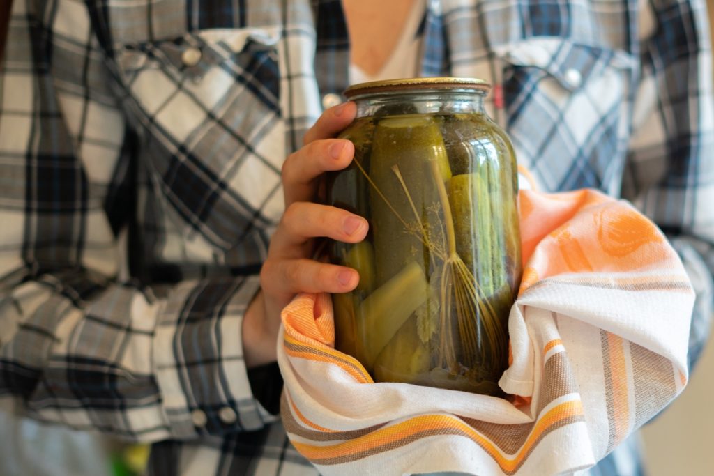 Femeie cu un borcan de castraveți murați fâșii în mâini