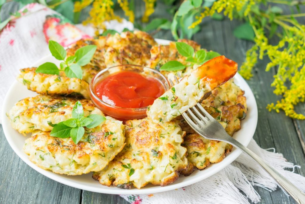 Chiftele de conopidă servite cu sos de roșii, una secționată, introdusă cu furculița în sos