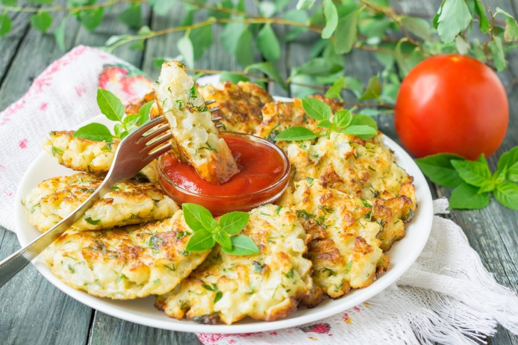 Chiftele de conopidă servite cu sos de roșii, una secționată, introdusă cu furculița în sos