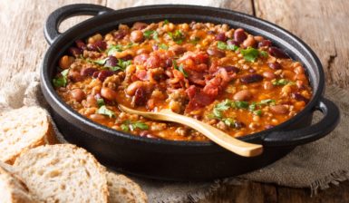 Iahnie de fasole cu bacon afumat în cratiță neagră cu lingură de lemn și felii de pâine