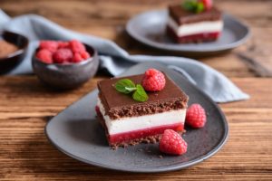 Două porții de prăjitură cu jeleu de zmeură și cremă de mascarpone și un bol cu zmeură