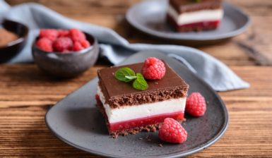 Două porții de prăjitură cu jeleu de zmeură și cremă de mascarpone și un bol cu zmeură