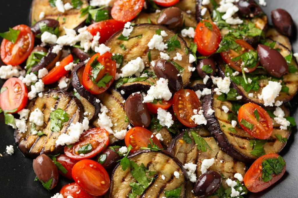 Rondele de vinete, măsline, felii de roșii, bucăți de brânză și frunze de pătrunjel