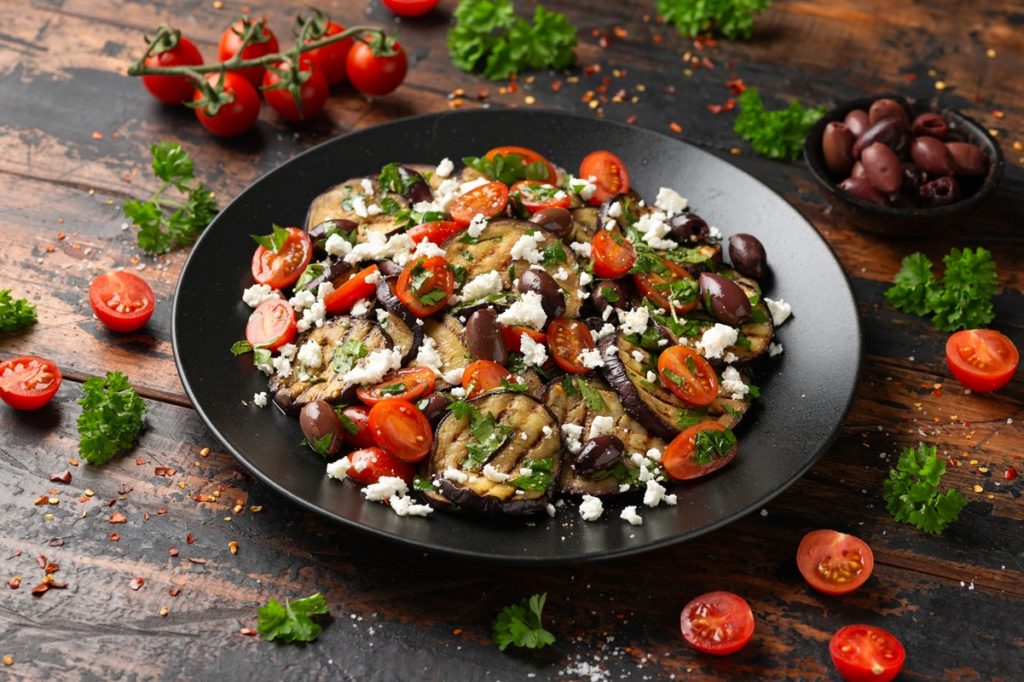 Vinete la grill cu măsline, roșii și brânză în farfurie adâncă, neagră