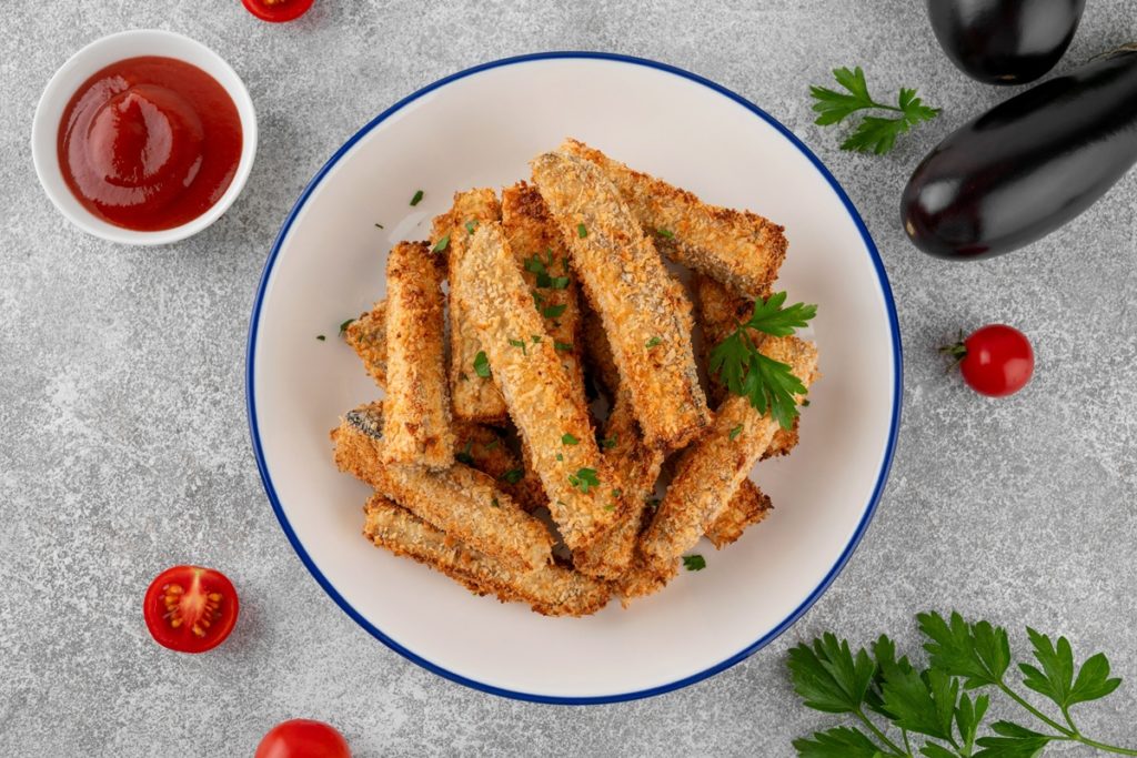 Sticksuri de vinete în crustă de pesmet cu parmezan alături de un bol cu sos de roșii