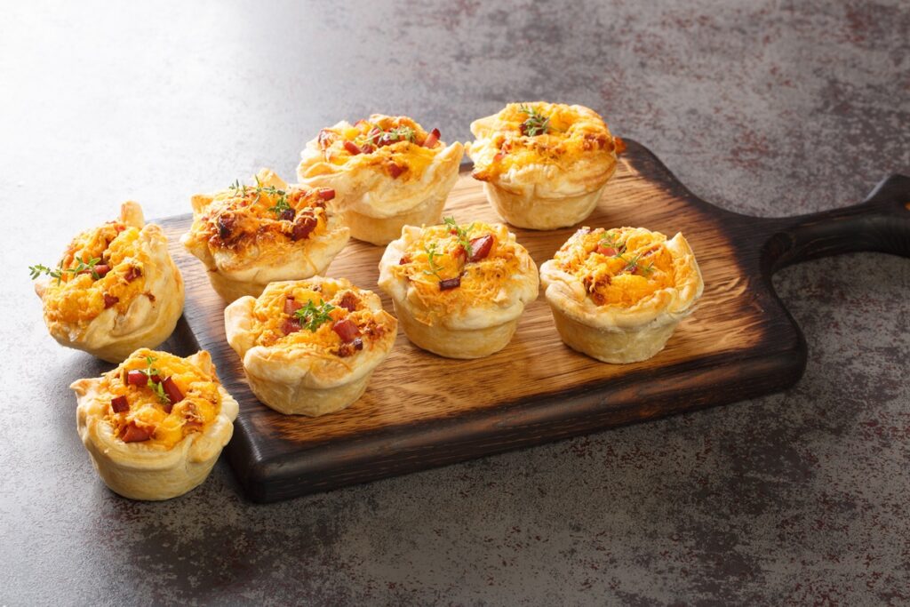 Coșulețe sărate din foietaj cu brânzeturi și bacon pe un tocător de lemn