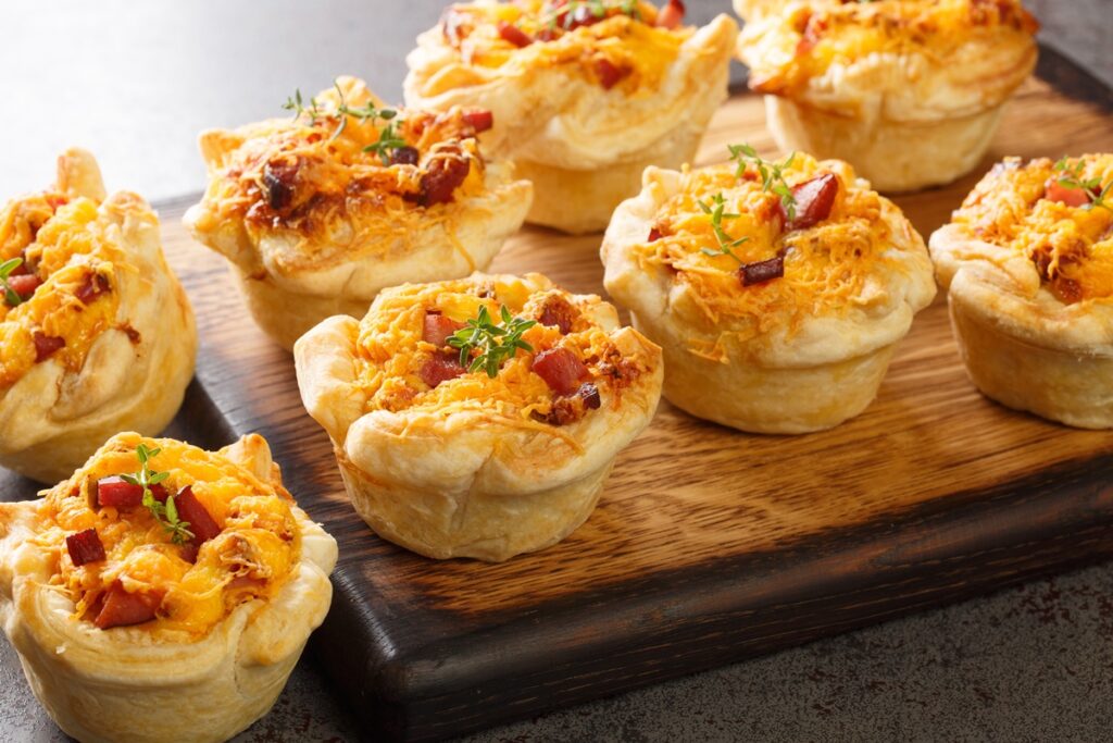 Coșulețe din foietaj cu brânzeturi și bacon pe un tocător de lemn