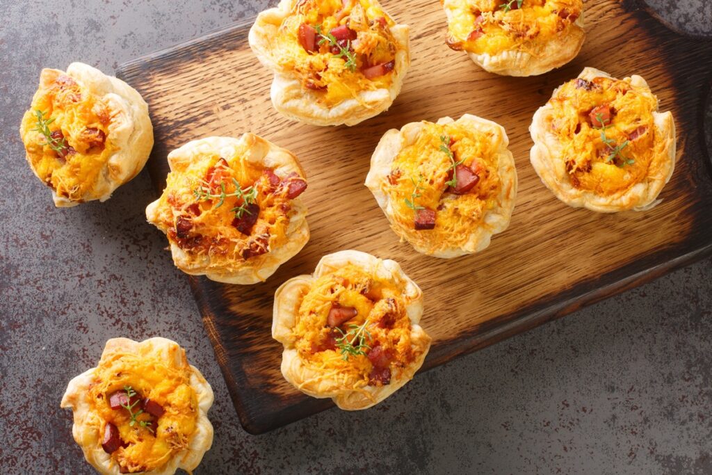 Coșulețe din foietaj cu brânzeturi și bacon pe un tocător de lemn