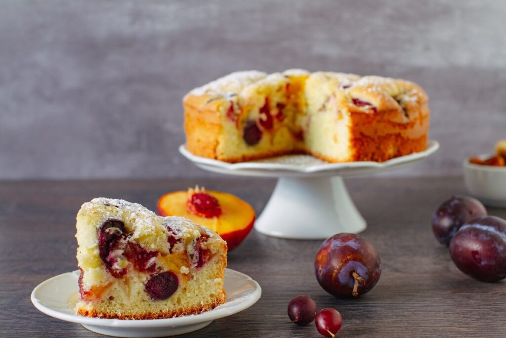 Pandișpan cu piersici, prune și merișoare porționat pe farfurie și pe platou