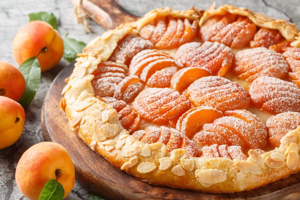 Galette cu caise în formă de evantai pe un tocător de lemn, alături de caise proaspete