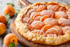 Galette cu caise în formă de evantai pe un tocător de lemn, alături de caise proaspete