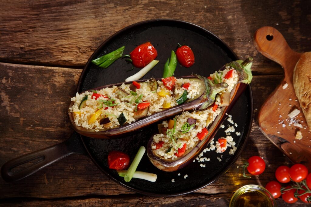 Două vinete umplute cu cușcuș și legume trase la tigaie, pe o farfurie neagră