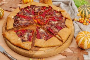 Galette cu dovleac în aluat și ardei copți cu brânză porționată pe un tocător de lemn