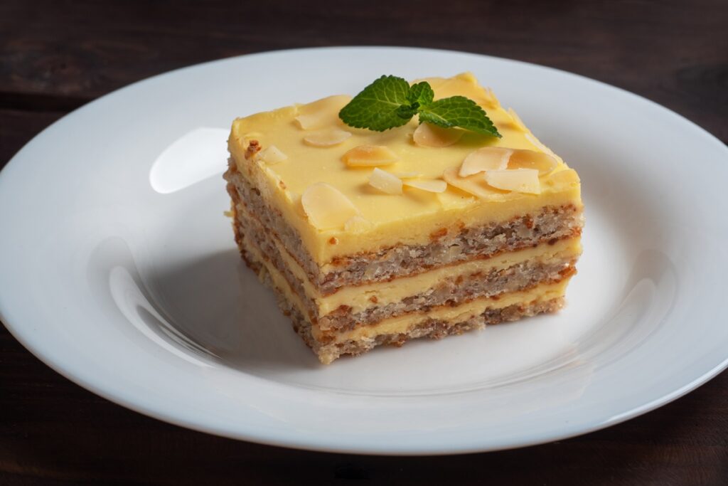 Porție de prăjitură cu blaturi din albușuri cu nuci și cremă de gălbenușuri