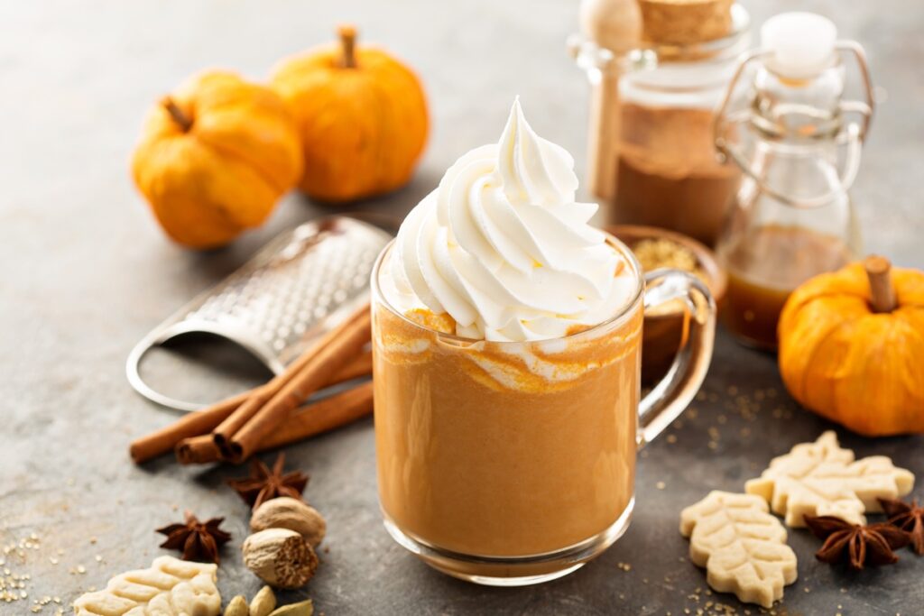 Pumpkin Spice Latte în cană, decorat cu frișcă, alături de dovleci, o răzătoare și condimente