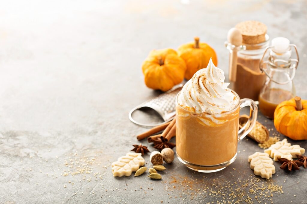 Pumpkin Spice Latte în cană, decorat cu frișcă, alături de dovleci și condimente