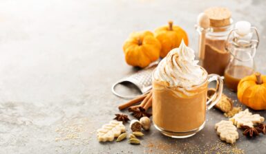 Pumpkin Spice Latte în cană, decorat cu frișcă, alături de dovleci și condimente