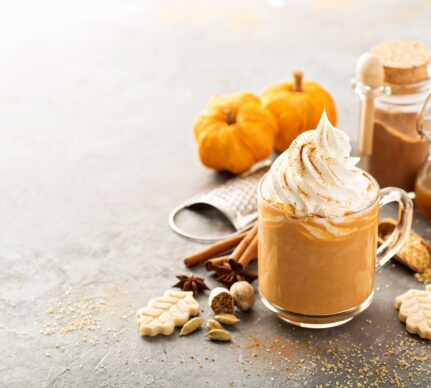 Pumpkin Spice Latte în cană, decorat cu frișcă, alături de dovleci și condimente