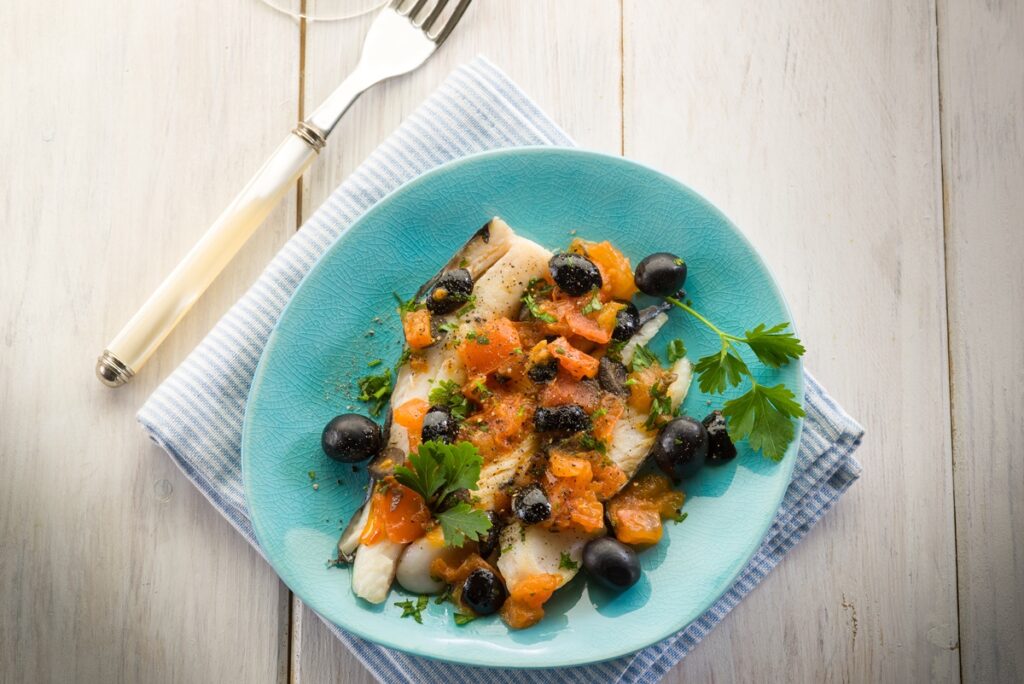 File de cod cu roșii și măsline negre în farfurie turcoaz și o furculiță