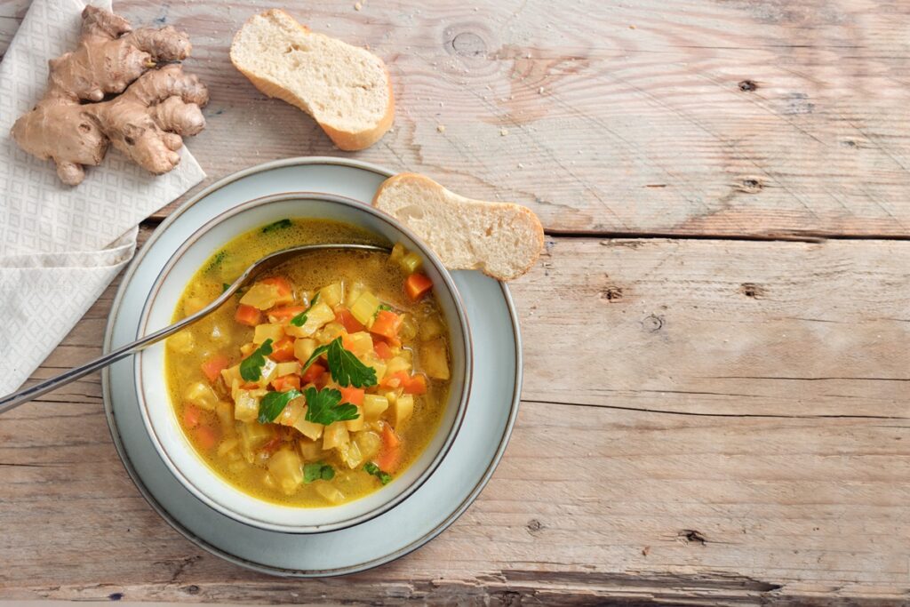 Supă de cartofi cu țelină apio și ghimbir în bol cu lingură, felii de pâine și o bucată de ghimbir