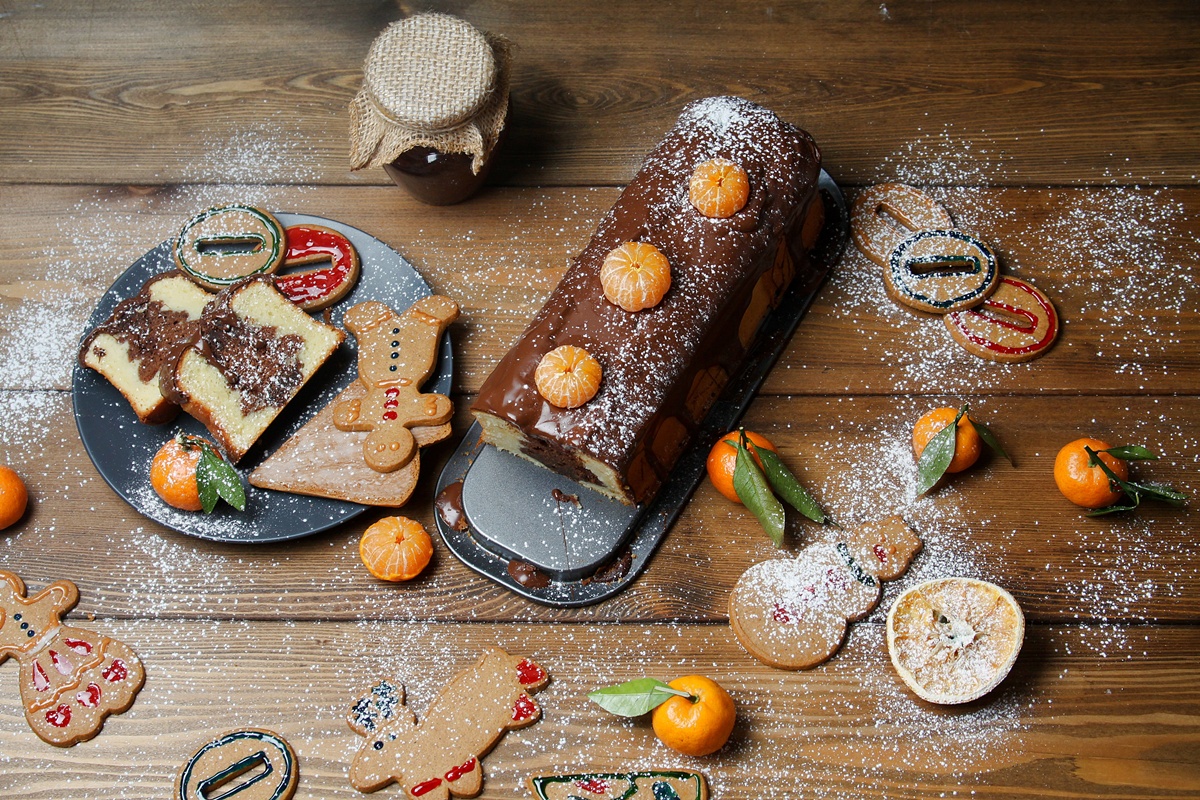 Chec festiv cu brăduț de ciocolată în interior, glazurat cu ciocolată și decorat cu mandarine porționat pe o farfurie și pe platou