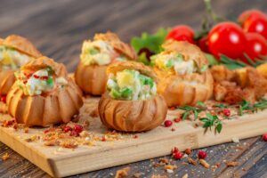 Choux-uri aperitiv umplute cu salată de legume cu maioneză pe un platou de lemn, cu roșii și salată verde